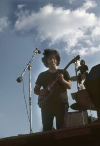 Jerry Garcia, guitarist for the Grateful Dead, playing on stage at the Sound Storm festival. An audience member is visible sitting on the scaffolding behind the stage. (Courtesy of Wisconsin Historical Society)