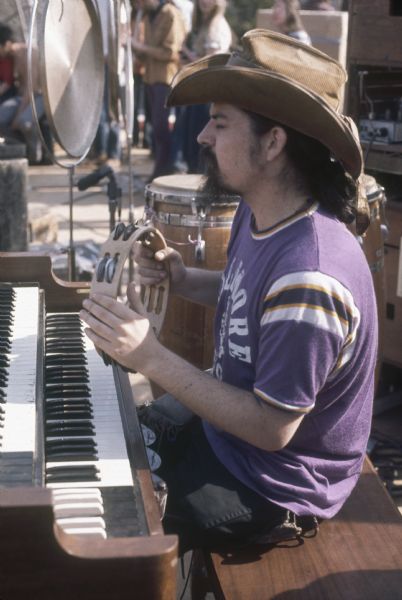Ron "Pigpen" McKernan, keyboardist and percussionist for the Grateful Dead, sitting at his keyboard mid-performance, playing a tambourine. His t-shirt reads "Fillmore East." (Courtesy of Wisconsin Historical Society)