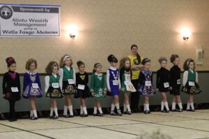 A group of younger Irish dancers wearing school dresses line up and prepare to compete in front of judges. (Photo by Molly McCollum)
