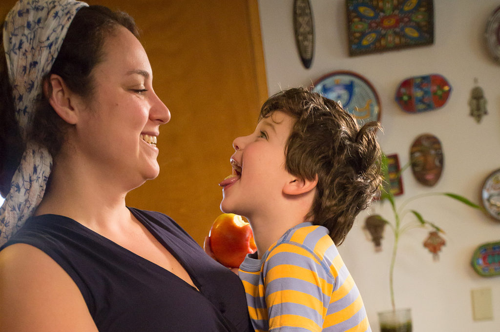 Laila and her young son smile at each other as the boy eats an apple