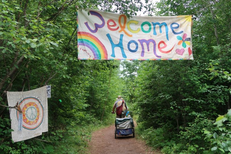 A sign reads “Welcome Home” at the beginning of the trail leading to the main meadow area of the Rainbow Family gathering on July 4, 2019. (Danielle Kaeding/WPR)