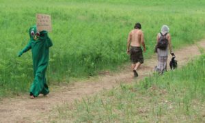 A person dressed in a Gumby costume holds a sign saying “Love One Another” at the Rainbow Family gathering on July 4, 2019. (Danielle Kaeding/WPR)