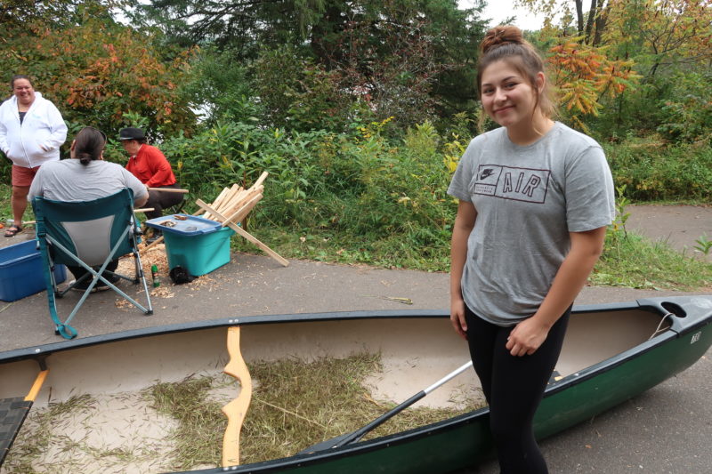 Seventeen year-old Kreighton Wolf is the chairwoman of the Bad River Youth Council. She stands next to a canoe filled with wild rice after harvesting on Pacwawong Lake. (Danielle Kaeding/WPR)