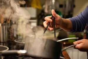 A close-up of hands sauteeing with chopsticks over a hot stove.