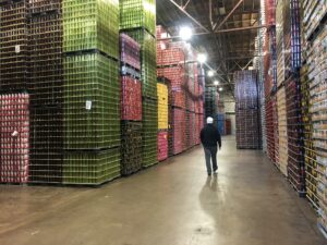 John Rassel, president of Krier Foods, walks in between stacks of cans at the Krier Foods warehouse in Random Lake, Wis. (Rachael Vasquez/WPR)