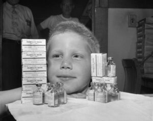 Child posing with polio vaccine bottles and boxes. (Courtesy of Wisconsin Historical Society)
