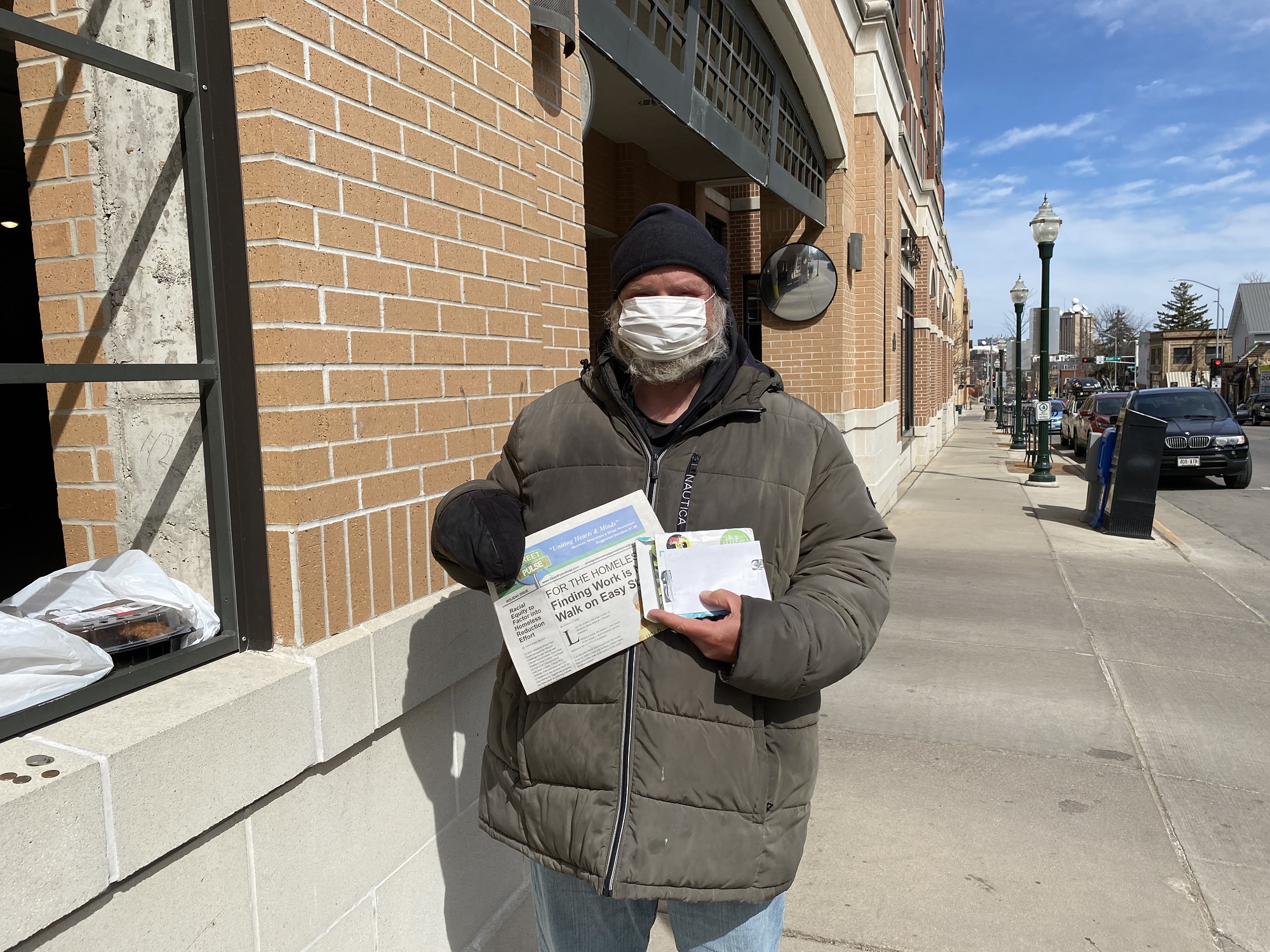 Chris Hubbard stands outside of Trader Joe’s in Madison on March 14, 2020, with the holiday issue of Street Pulse newspaper and some photography prints. It was his 52nd birthday. (Alyssa Allemand/WPR) 