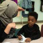 Nida Malik, a head teacher at Crescent Learning Center, talks with one of her students while he is coloring.