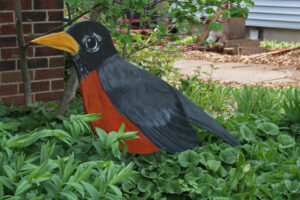 Wooden painted robin sits in a front yard.