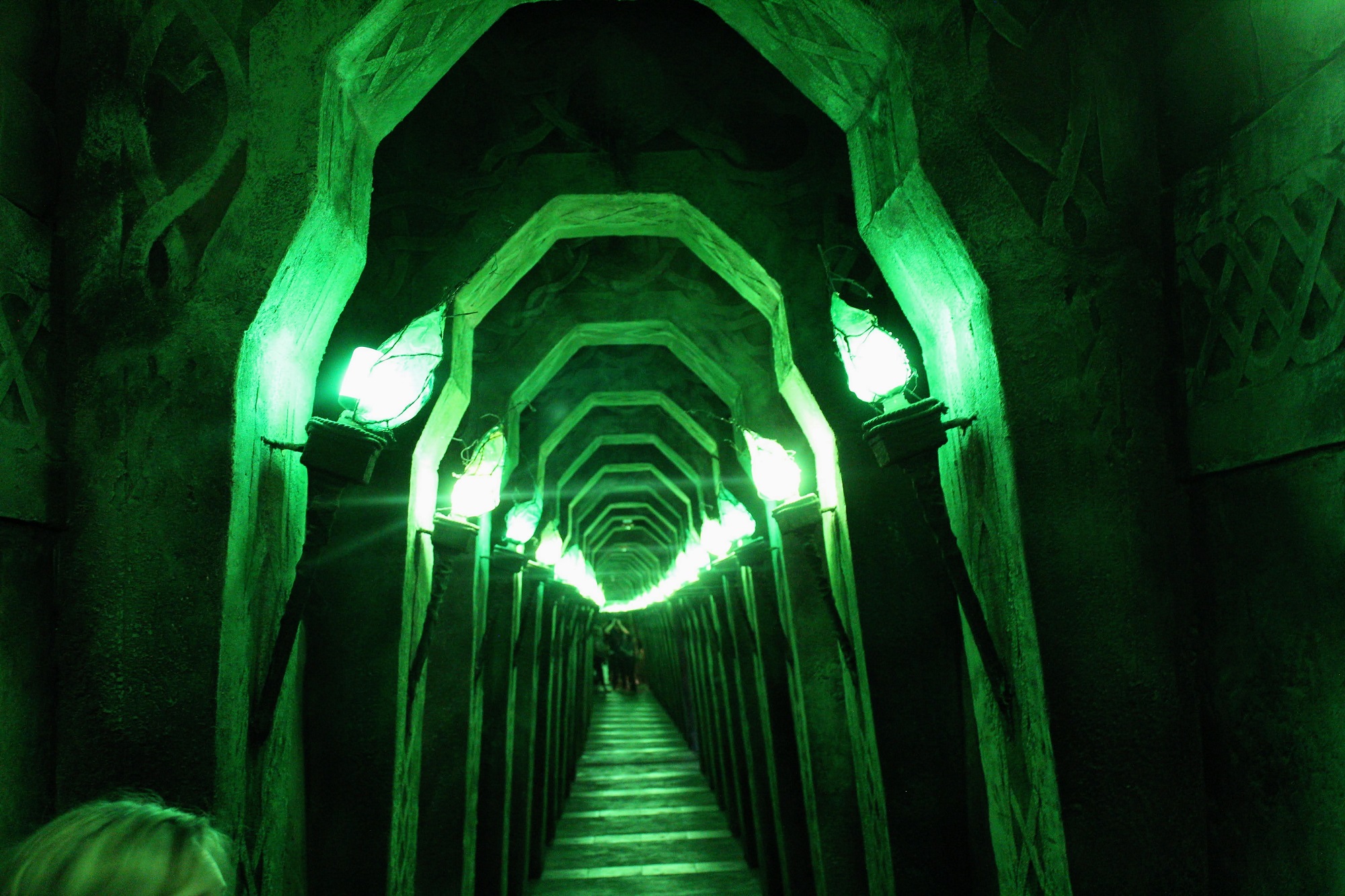  In the earth realm of Wizard Quest, there is a deep green corridor lined with Celtic arches and flickering green torches. While mirrors on both ends produce the illusion that the hallway is endless, Corena Ricks says the actual hallway is only around 30 feet long – but visitors aren't aware of how long it really goes until they reach the mirror at the end. (Trina La Susa/WPR)