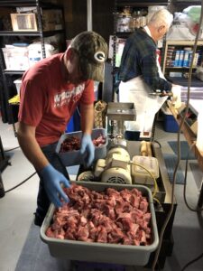 Scott Jahnke loads venison and local pork into the grinder. His dad, Bob Jahnke, preps the air-powered stuffer. (Photo by Briana Rupel)