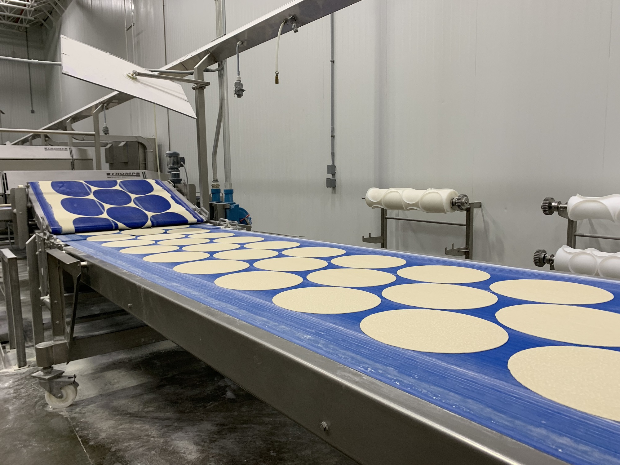 Inside Bernatello’s facility a machine rolls dough flat and cuts out pizza-sized circles for baking. (Photo by Jana Rose Schleis)