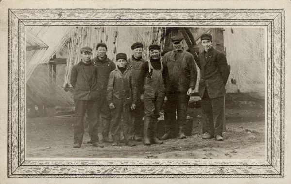Fishermen from the Frank Braeger fishing tugboat are standing for a group portrait in front of their fishing nets on Jones Island.
