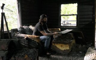 Comedian Jacy Catlin sits in the living room of his burned house outside Osseo, Wisconsin. (Courtesy of Jacy Catlin)