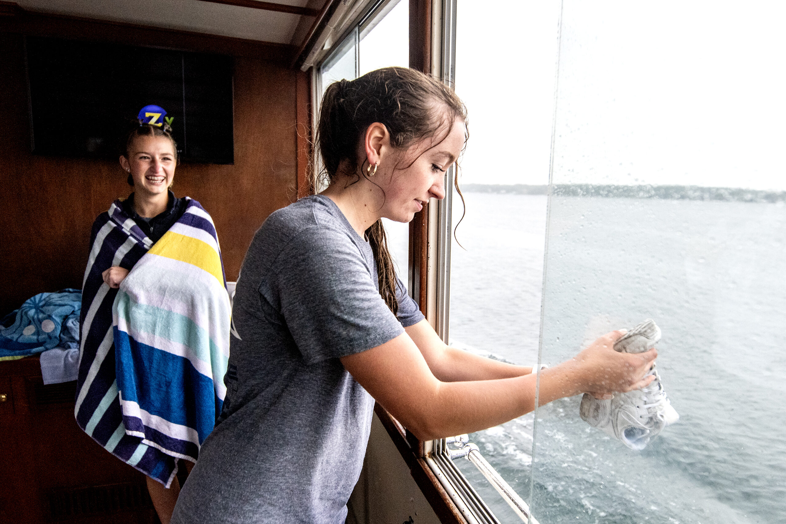 Hailey Osborne, center, and Emma Bond, left, try to dry off after falling into the lake due to rainy weather during mailboat jumping tryouts Tuesday, June 13, 2023, in Lake Geneva, Wis. (Angela Major/WPR)