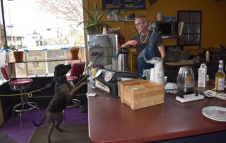The Victory café owner Patrick Downey tosses a piece of ham to a dog over the counter on April 28, 2023. (Alyssa Allemand/WPR)