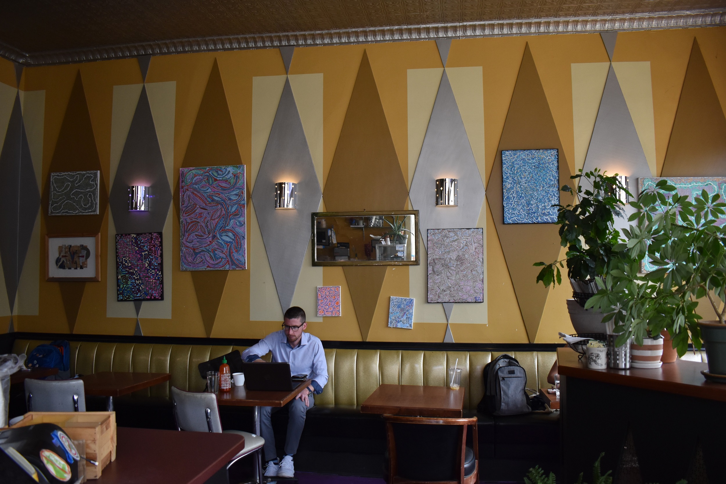 A customer works on a laptop at one of the tables at The Victory. The walls are filled with gold and silver diamonds and feature owner Patrick Downey's artwork that can be purchased. (Alyssa Allemand/WPR)