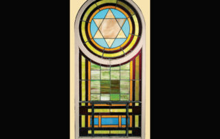 The White Shul’s Star of David window features blue, brown, and green glass in a circular pattern around a light brown Star of David. Below that is a pattern of green, brown, and blue glass in rectangular shapes. The entire piece is enclosed in a wooden frame. (Courtesy of the Wisconsin Historical Society)
