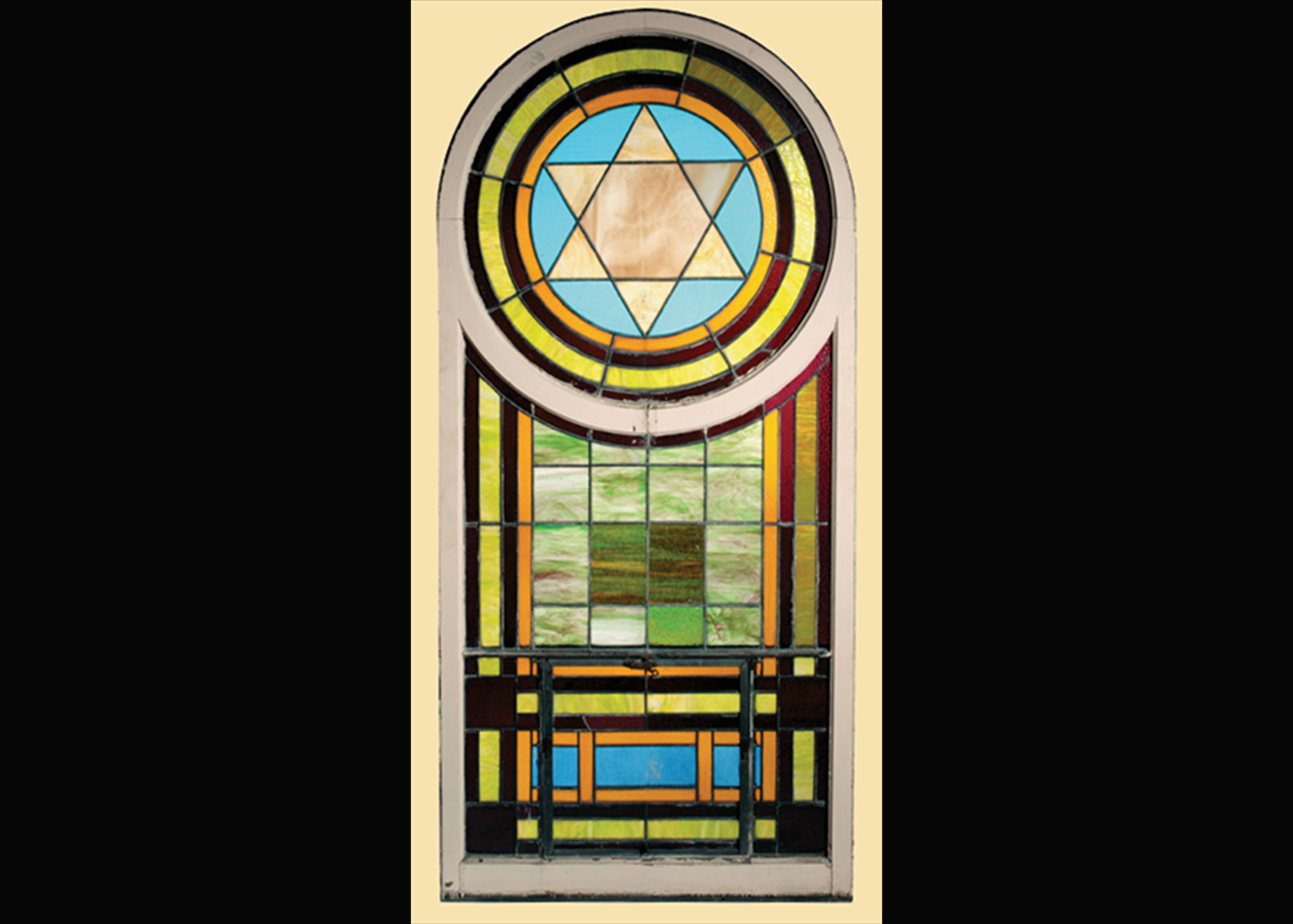 The White Shul’s Star of David window features blue, brown, and green glass in a circular pattern around a light brown Star of David. Below that is a pattern of green, brown, and blue glass in rectangular shapes. The entire piece is enclosed in a wooden frame. (Courtesy of the Wisconsin Historical Society)