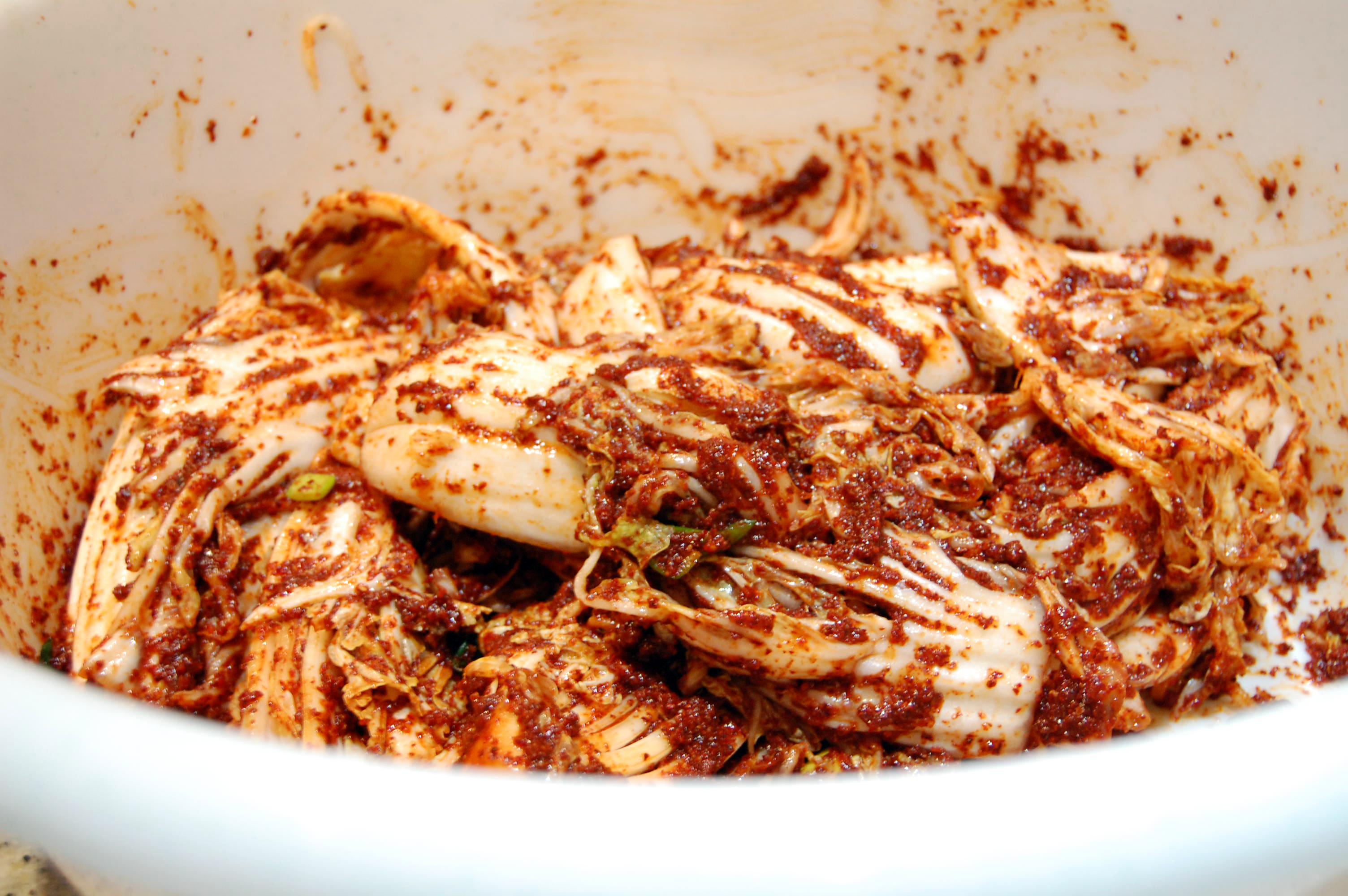 Cabbage leaves covered with kimchi paste rest in a large bowl.