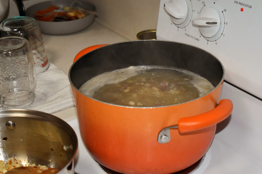 A pot of broth mixed with pork neck bones, beans and onions simmers on the stove on Dec. 21, 2023. (Danielle Kaeding/WPR)