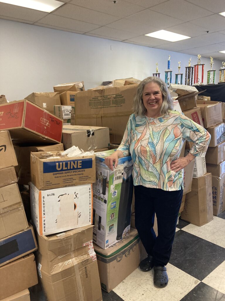 Janet Gray, co-founder of Nationwide Trophy Recycling, in front of the boxes of unopened trophies waiting to be recycled. (Photo by Alexandra Salmon)