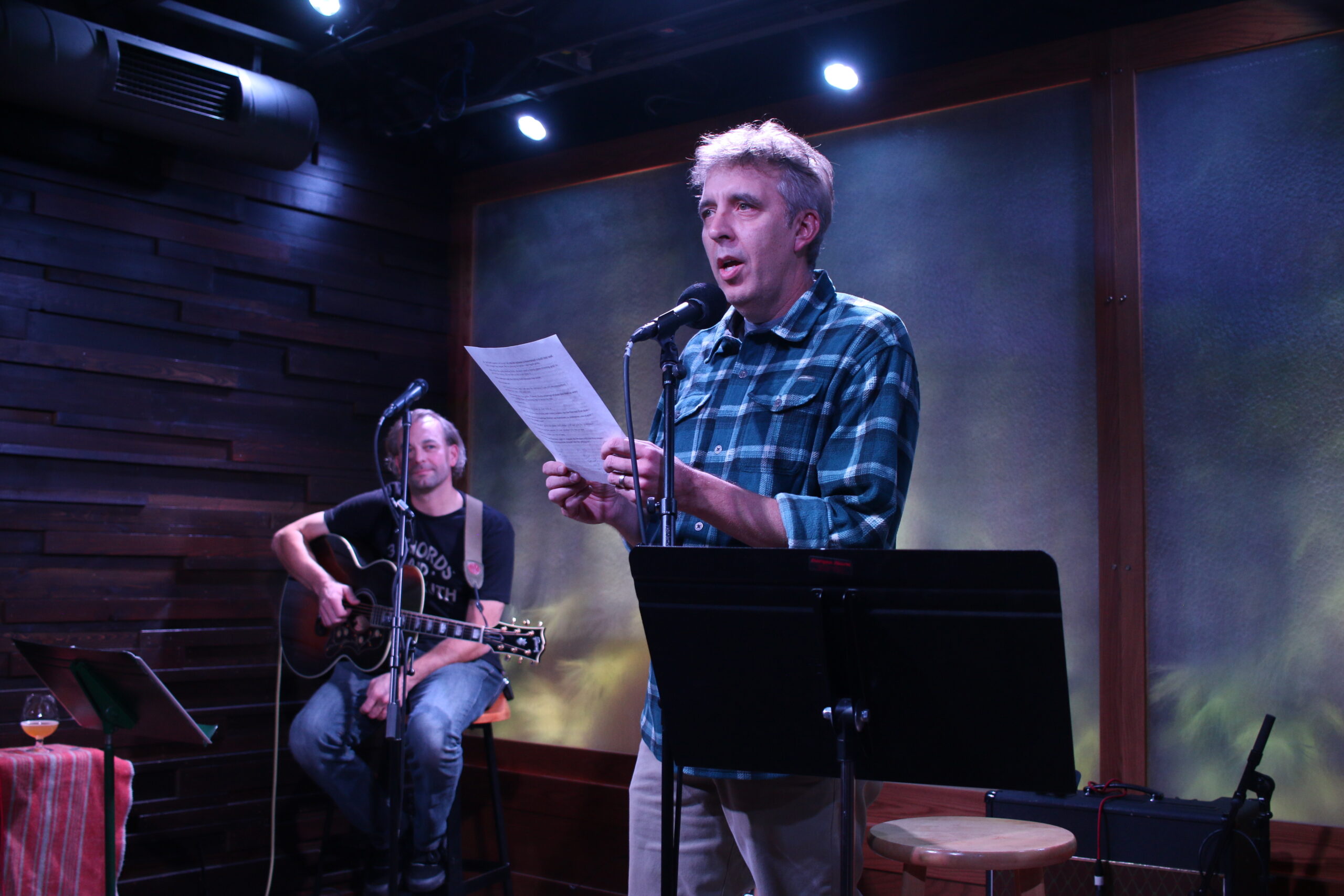 Writer Ken Szymanski, right, of Eau Claire, shares the story, “Built to Last” at The Lakely in Eau Claire on Nov. 14, 2024. Musician Derick Black, left, played guitar between storytellers. The storytelling event was hosted by WPR’s “Wisconsin Life” and the Chippewa Valley Writers Guild. Rich Kremer/WPR